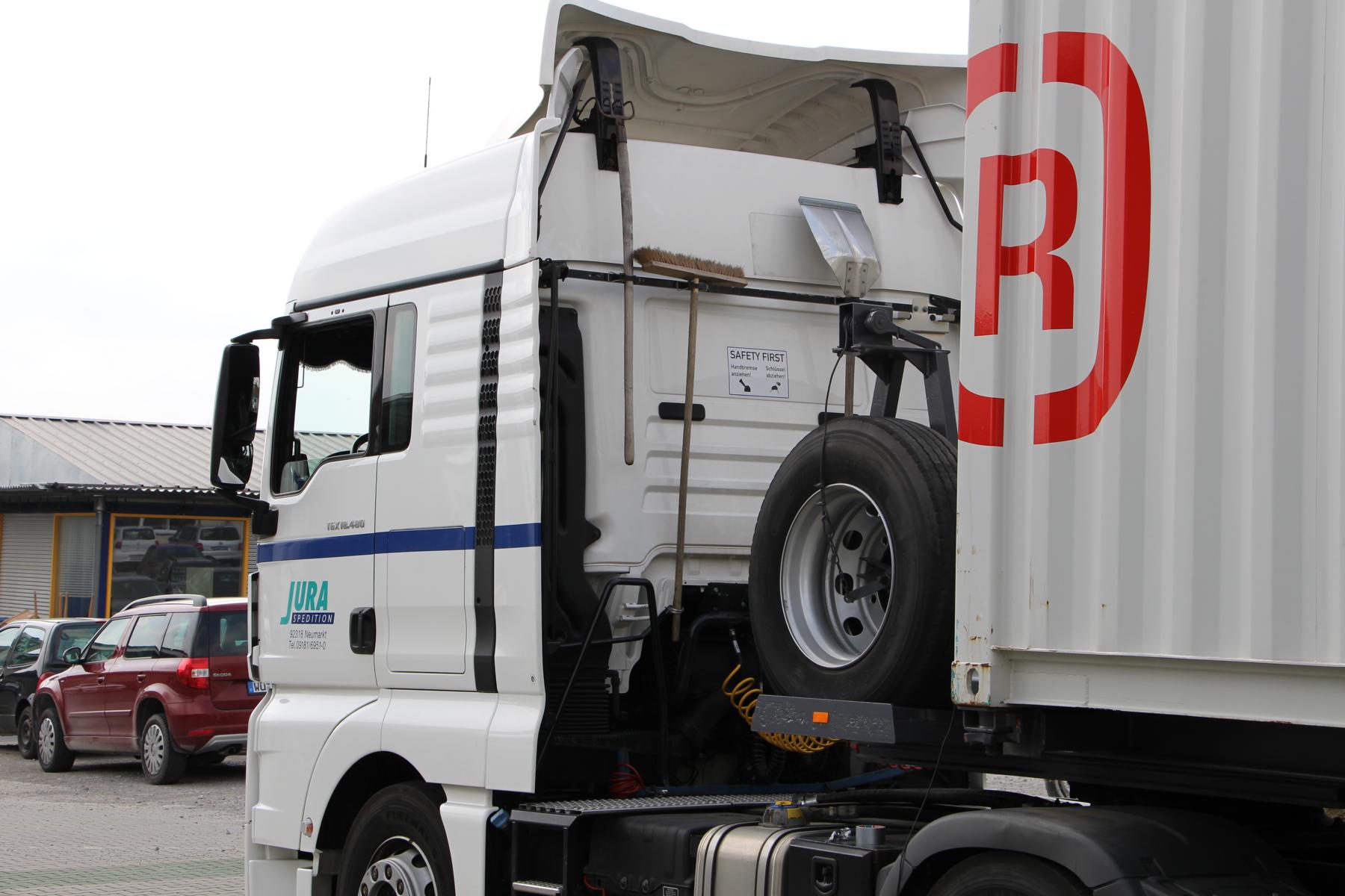 Een vrachtwagen met een container op een wagen en het logo van Rothschenk op het bedrijfsterrein.