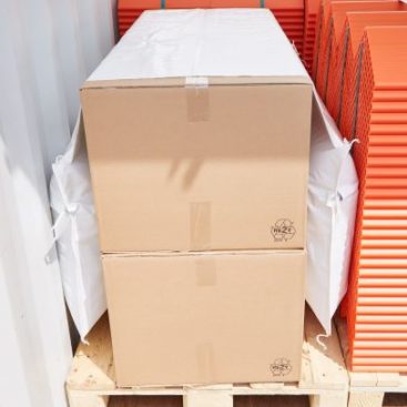 Een zadeltas met twee stuwblokken aan de zijkant zet kartonnen dozen vast op een pallet in een container. Organische randbeschermers worden ernaast vastgezet.