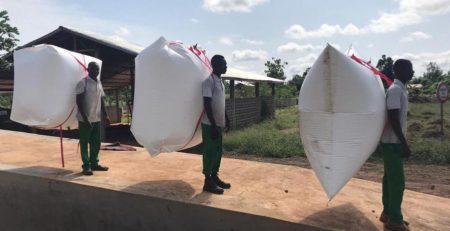 Three Africans with biogas backpacks on their backs stand on a ramp.