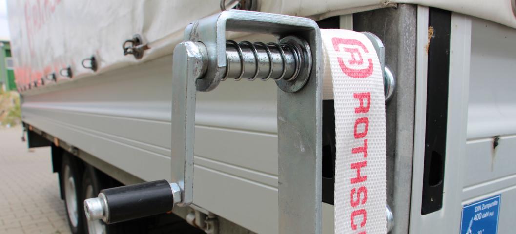 Transport van bouwmateriaal - Een oprolmechanisme voor spanbanden op een vrachtwagen met een spanband met Rothschenk-logo.